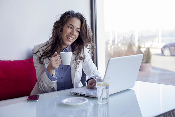 Mujer sonriente tomando un taza café por la mañana y usando una laptop